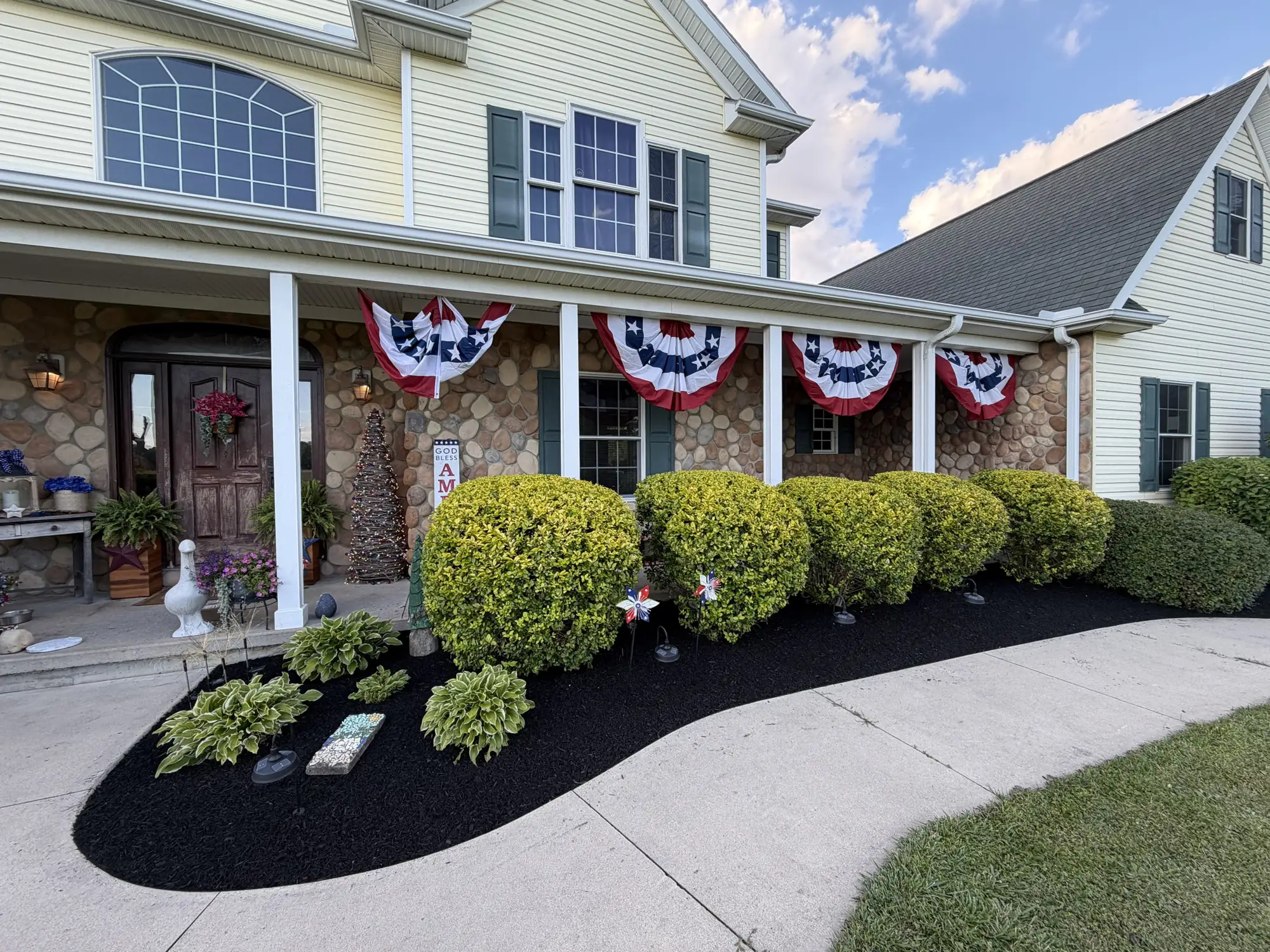 Freshly mulched beds with trimmed shrubs along a covered stone porch and concrete walkway